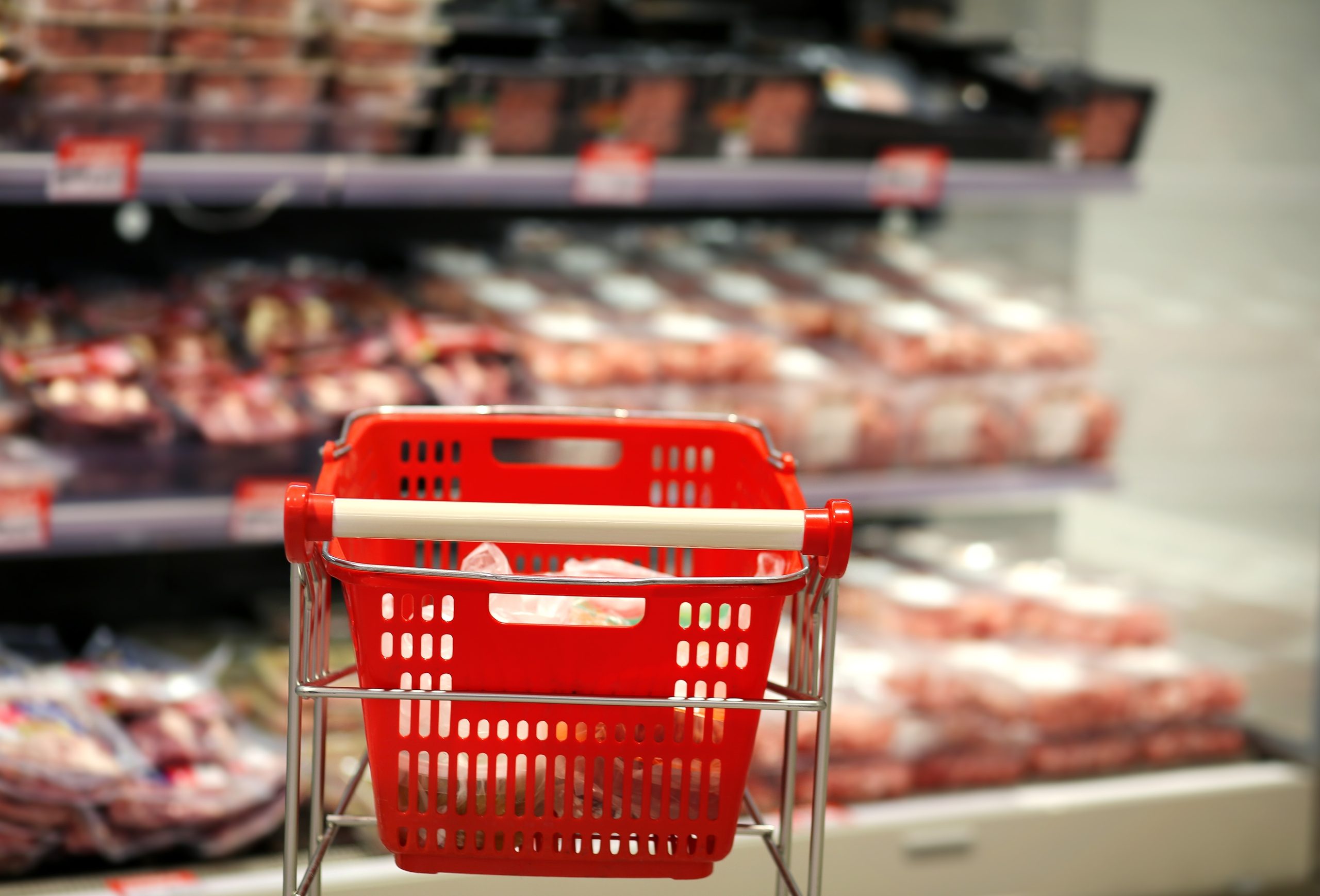Das Bild zeigt einen Einkaufswagen vor einem Fleischregal im Supermarkt.